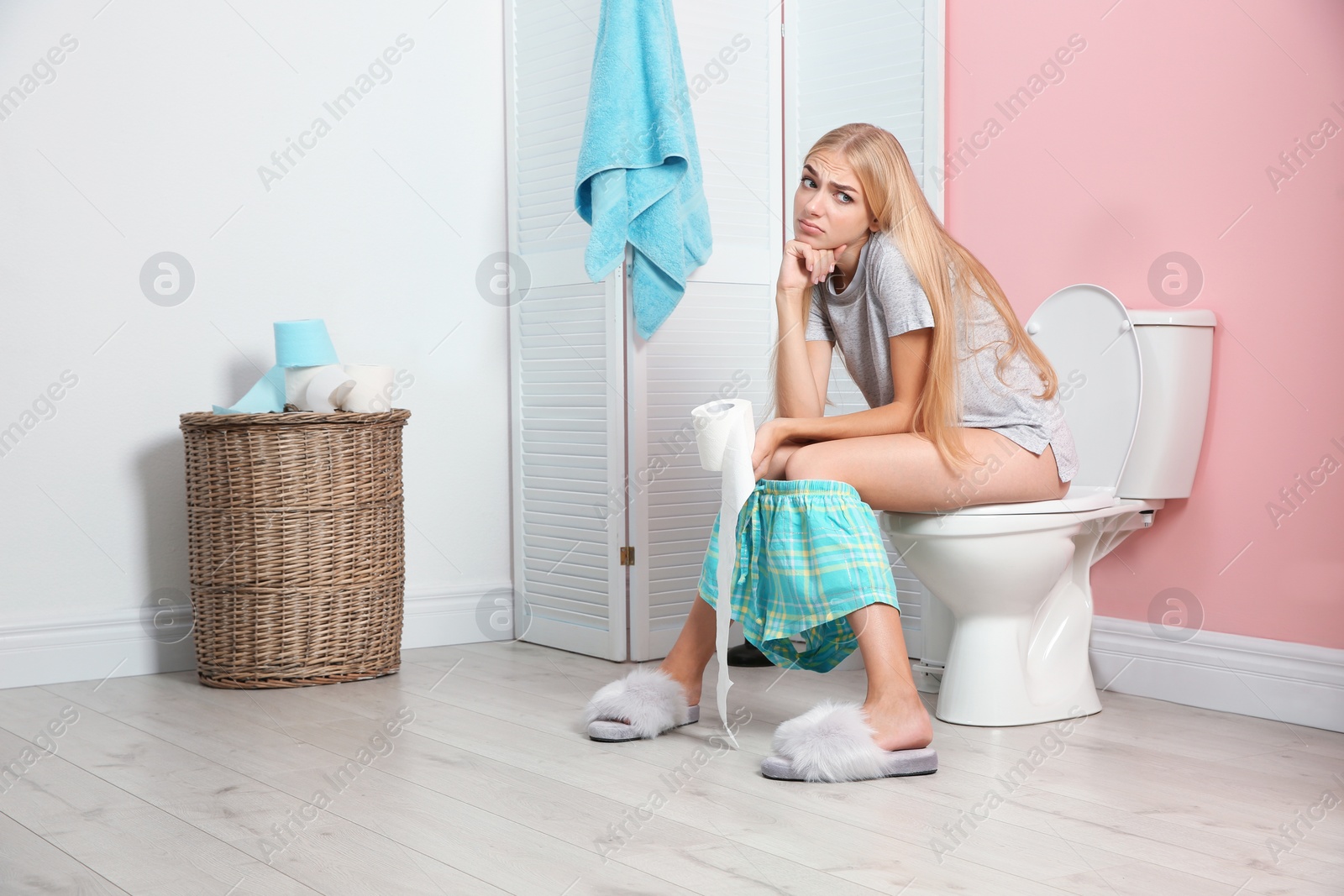 Photo of Woman with paper roll sitting on toilet bowl in bathroom