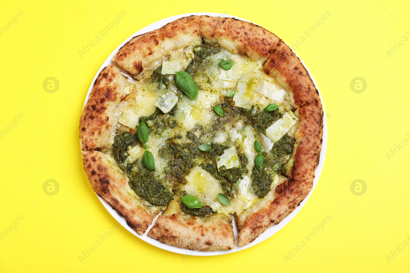 Photo of Delicious pizza with pesto, cheese and basil on yellow background, top view