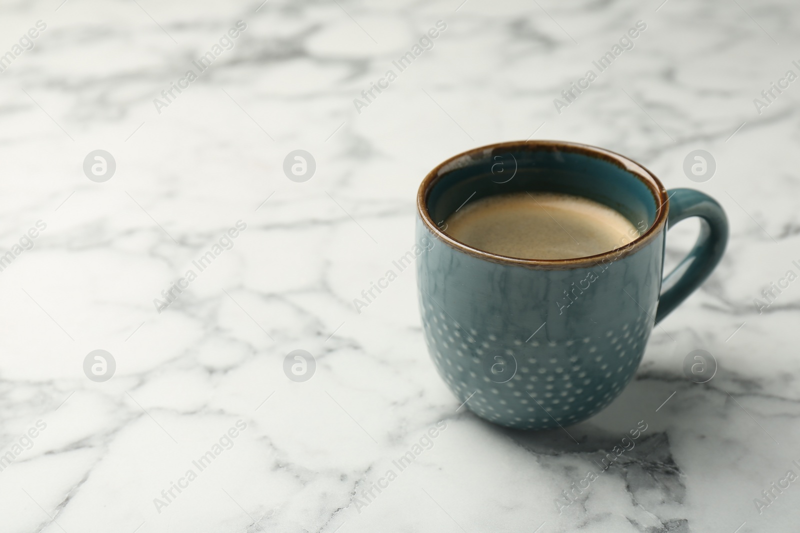 Photo of Tasty coffee in cup on white marble table. Space for text