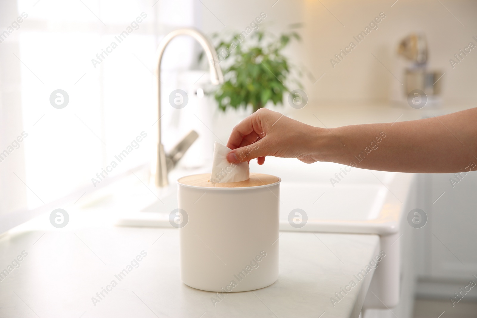 Photo of Woman taking paper tissue out of box on white countertop in kitchen, closeup