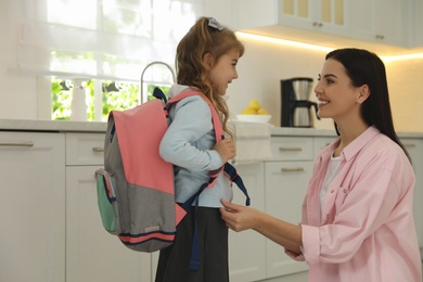 Photo of Young mother helping her little child get ready for school in kitchen