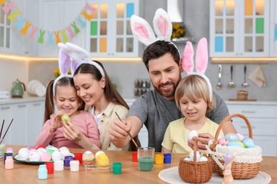 Photo of Happy family painting Easter eggs at table in kitchen