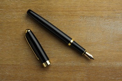 Stylish fountain pen and cap on wooden table, flat lay