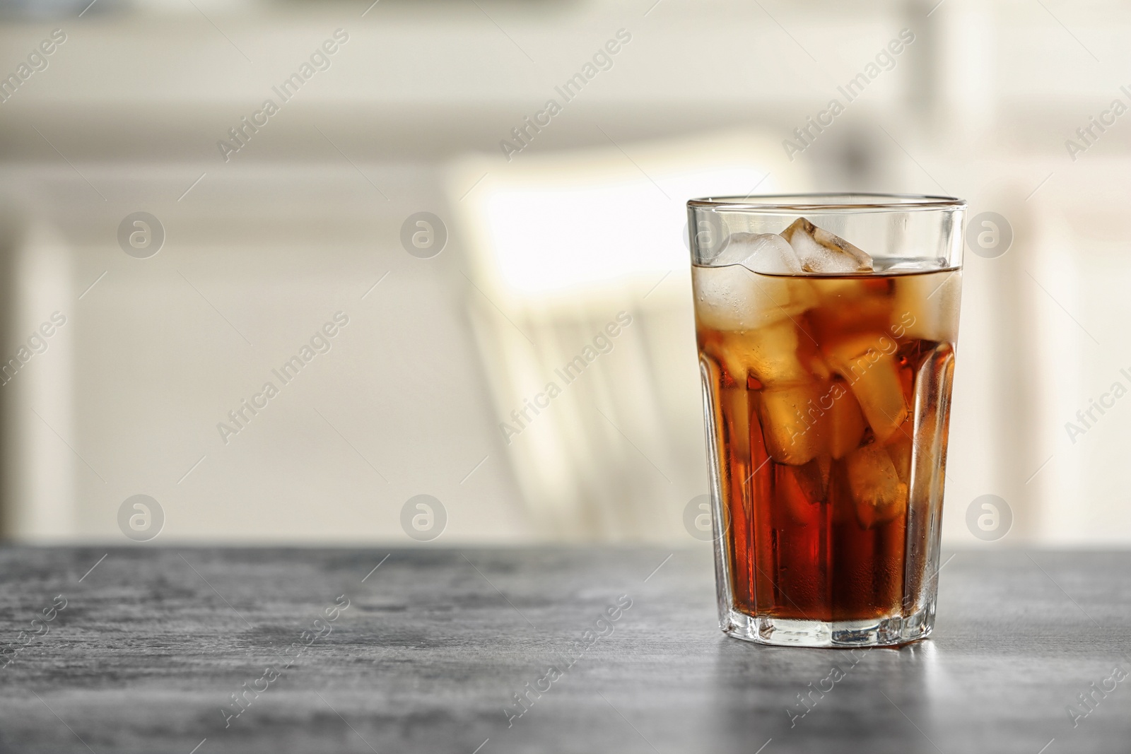 Photo of Glass of cola with ice on table against blurred background, space for text