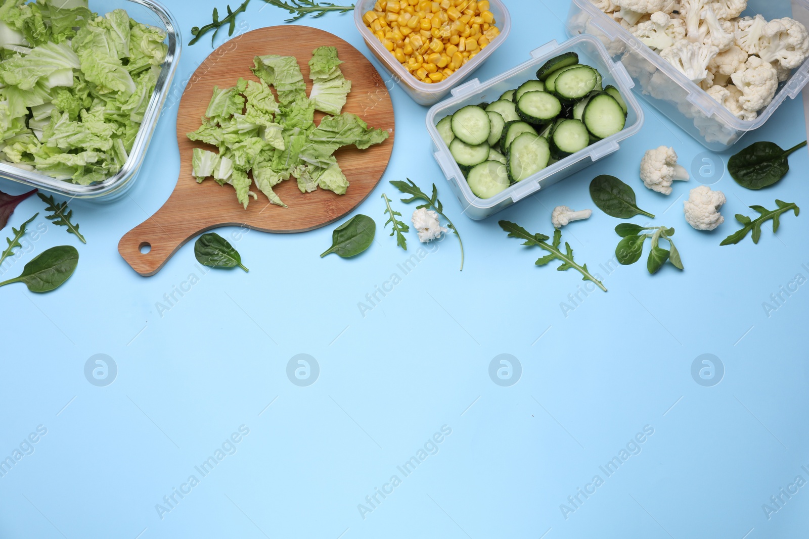 Photo of Different containers and wooden board with fresh products on light blue background, flat lay. Space for text