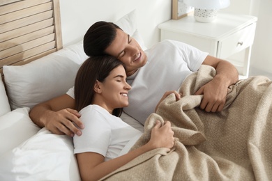 Photo of Happy couple covered with warm beige plaid sleeping in bed indoors