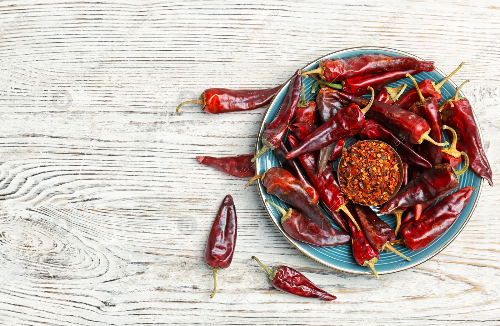 Photo of Plate with dry chili peppers and powder on wooden background