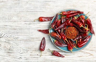 Plate with dry chili peppers and powder on wooden background