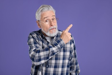 Photo of Surprised senior man pointing at something on violet background