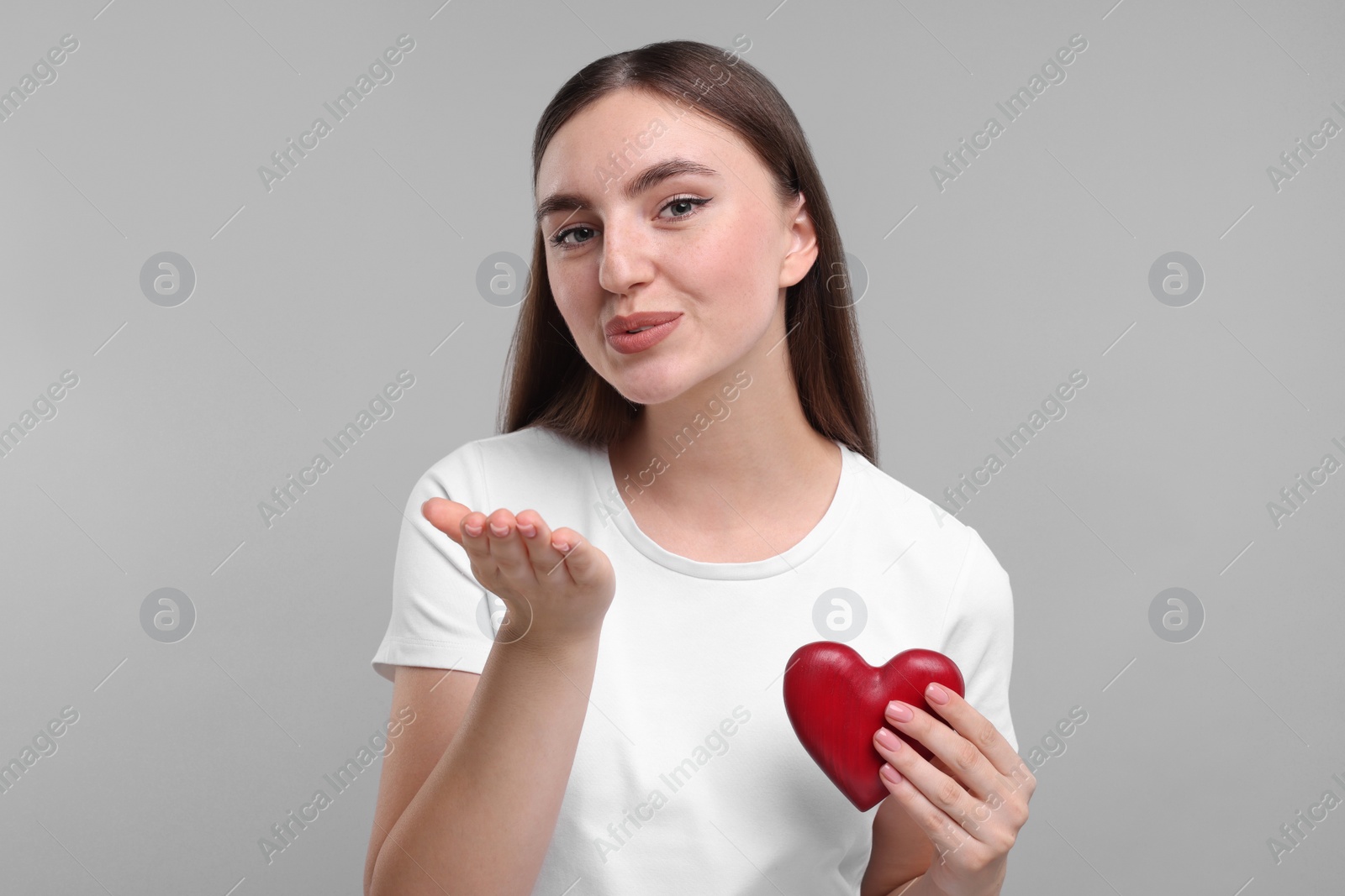 Photo of Beautiful woman holding red heart and blowing kiss on light grey background