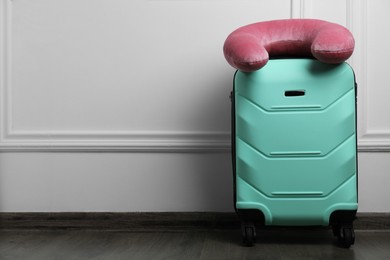 Photo of Pink travel pillow on turquoise suitcase near white wall indoors, space for text