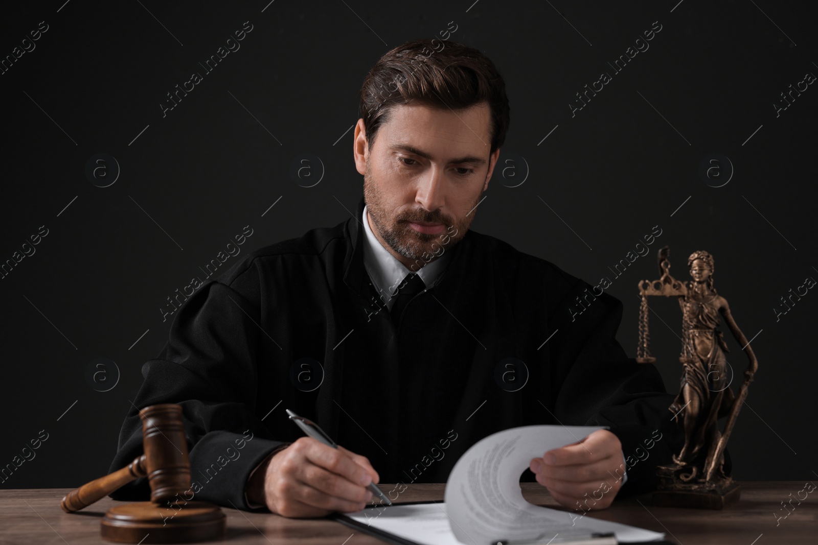 Photo of Judge with gavel writing in papers at wooden table against black background