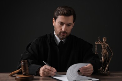 Judge with gavel writing in papers at wooden table against black background