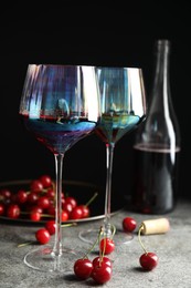 Photo of Delicious cherry wine and ripe juicy berries on grey table against black background