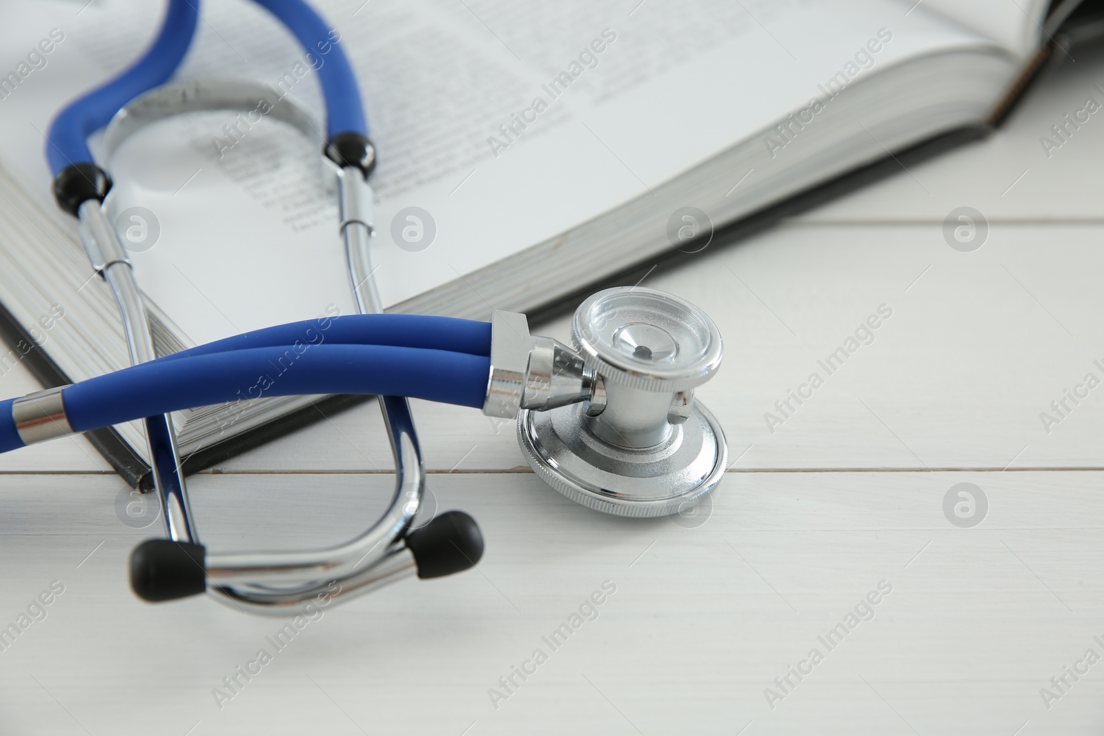 Photo of One medical stethoscope and book on white wooden table, closeup