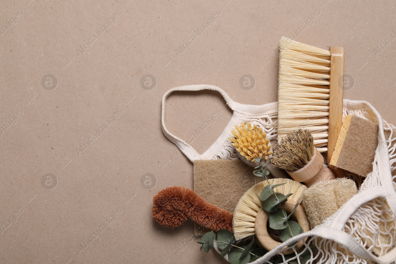 Photo of Cleaning brushes, sponges, eucalyptus and string bag on pale brown background, top view. Space for text