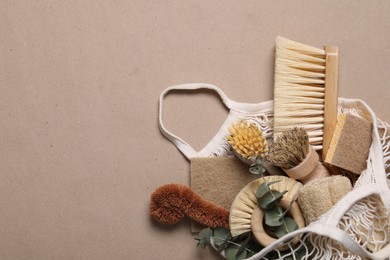 Photo of Cleaning brushes, sponges, eucalyptus and string bag on pale brown background, top view. Space for text