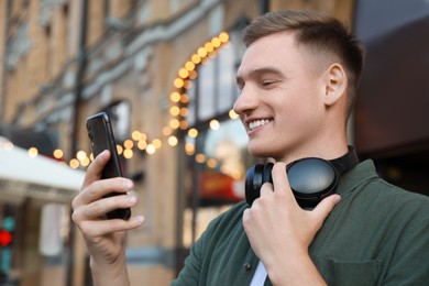 Smiling man with headphones using smartphone outdoors