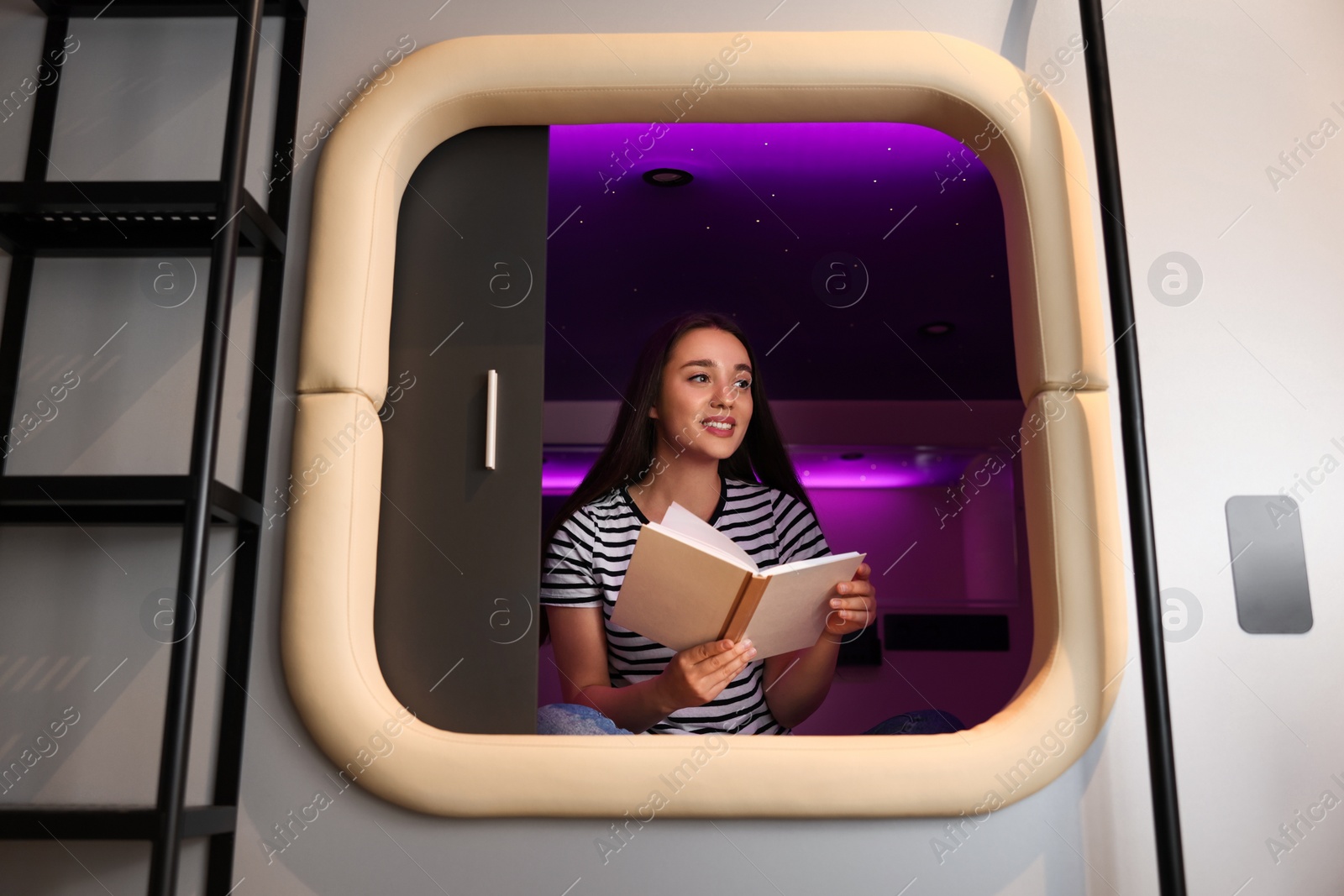 Photo of Happy young woman reading book in capsule of pod hostel