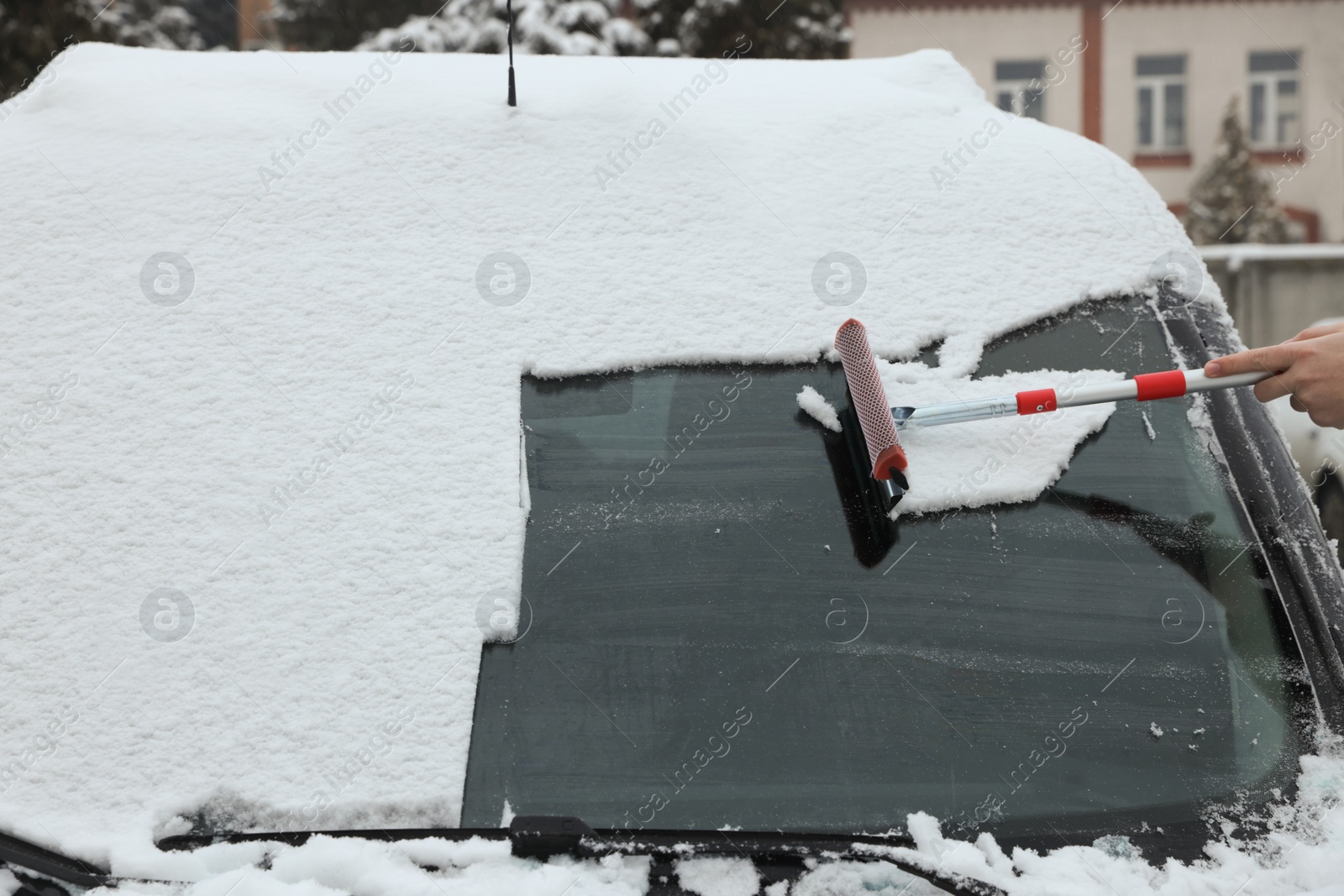 Photo of Woman cleaning car windshield from snow with squeegee outdoors, closeup