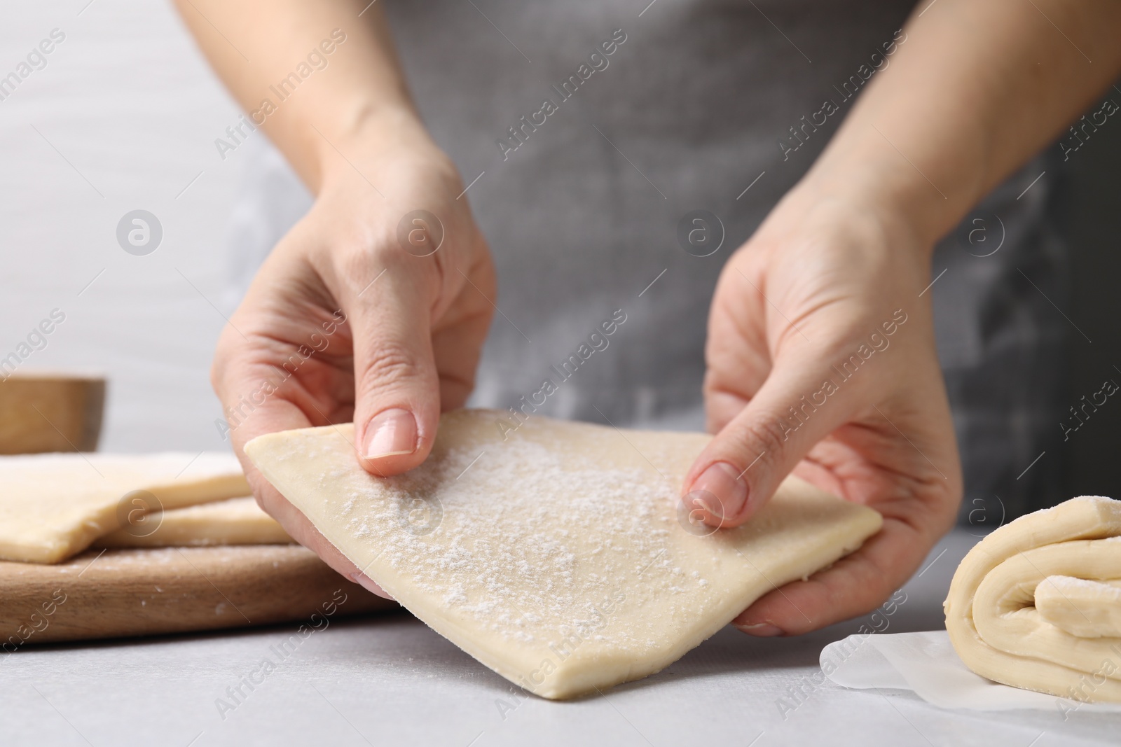 Photo of Woman with raw puff pastry dough at white table, closeup