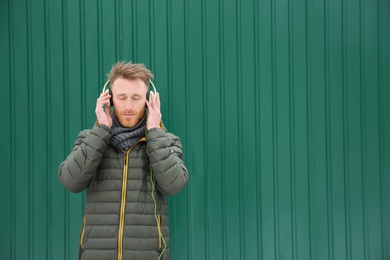 Photo of Young man listening to music with headphones against color wall. Space for text