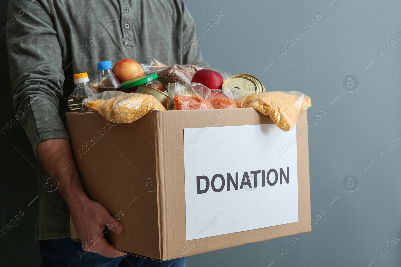 Photo of Man holding donation box with food on gray background, closeup