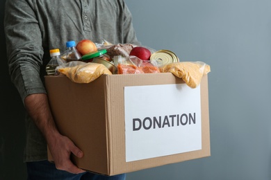 Photo of Man holding donation box with food on gray background, closeup