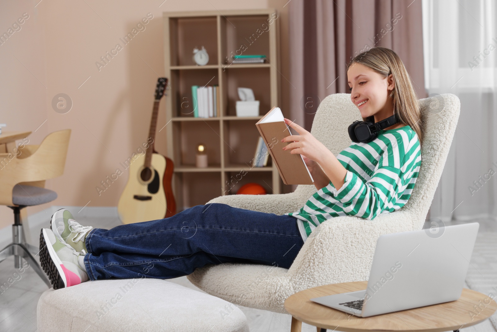 Photo of Online learning. Teenage girl reading book near laptop at home