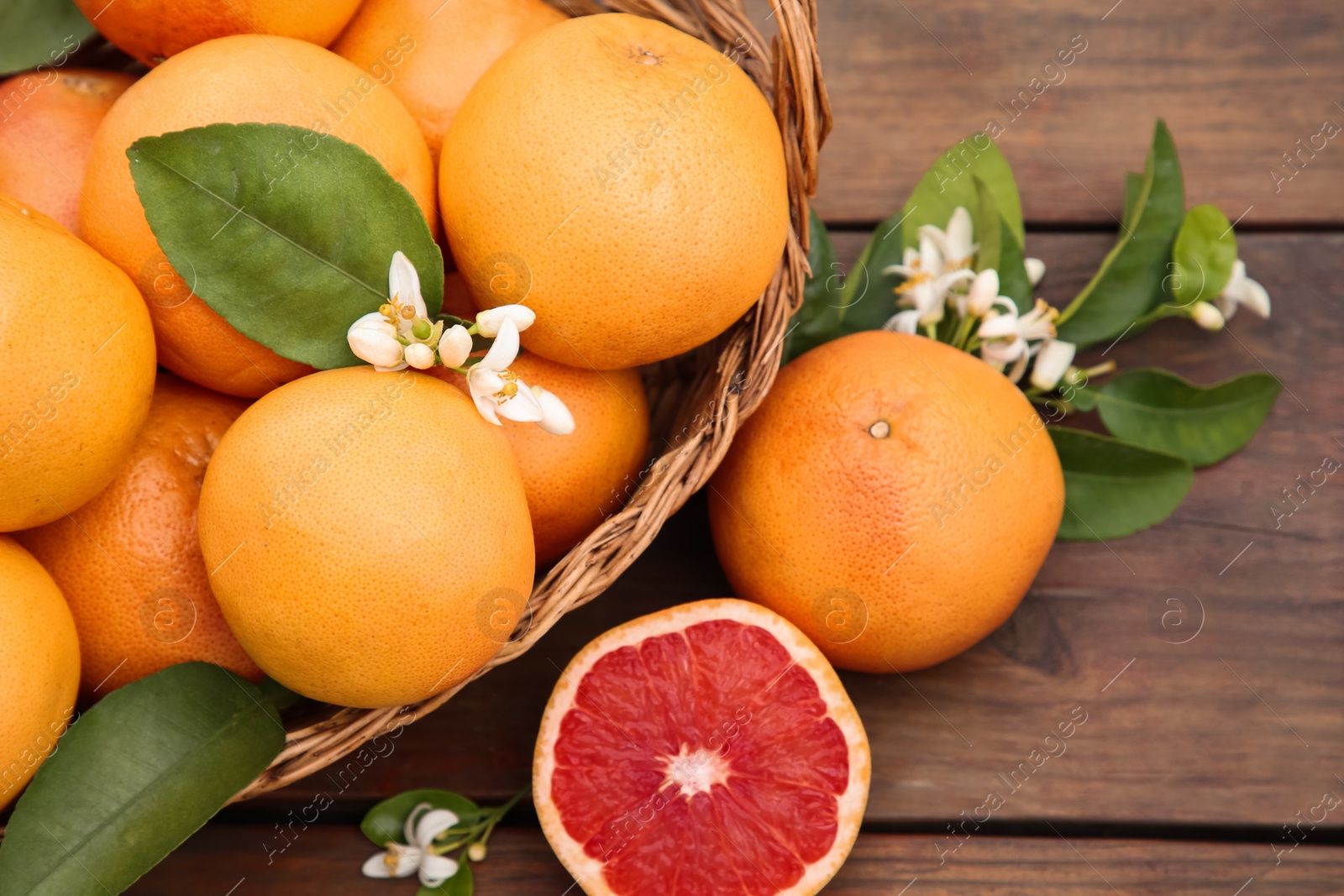 Photo of Wicker basket with fresh grapefruits and green leaves on wooden table