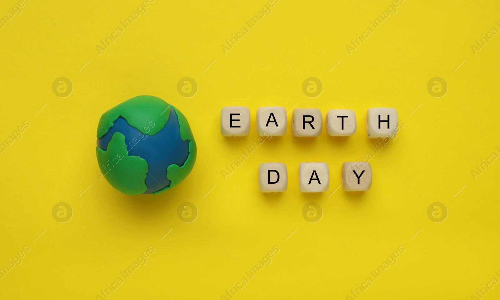 Photo of Plasticine model of planet and phrase Earth Day on yellow background, flat lay