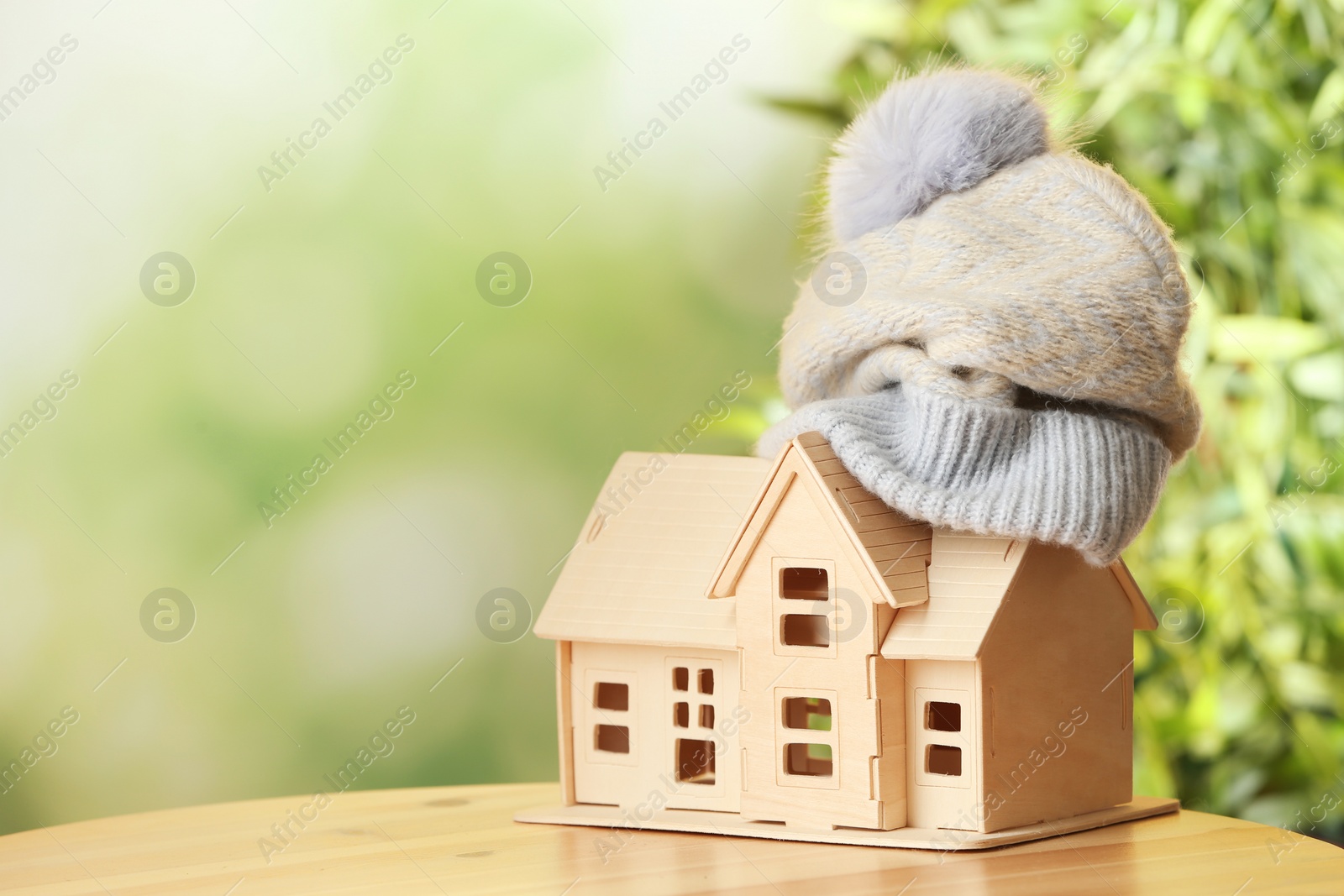 Photo of House model and hat on wooden table against blurred background, space for text. Heating efficiency