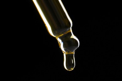 Photo of Dripping tincture from pipette on black background, closeup