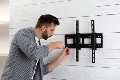 Photo of Man with screwdriver installing TV bracket on wall indoors