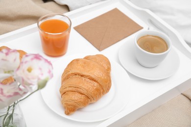 Photo of Tray with tasty croissant, drinks and flowers on bed