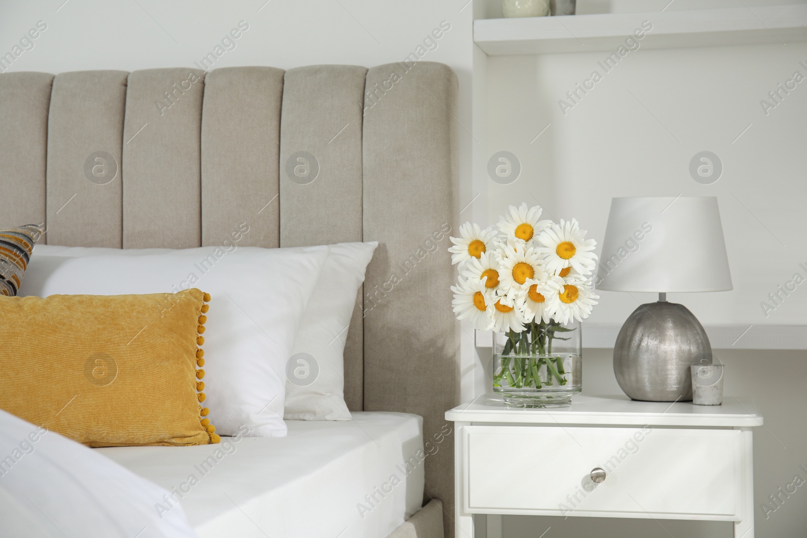 Photo of Bouquet of beautiful daisy flowers and lamp on nightstand in bedroom
