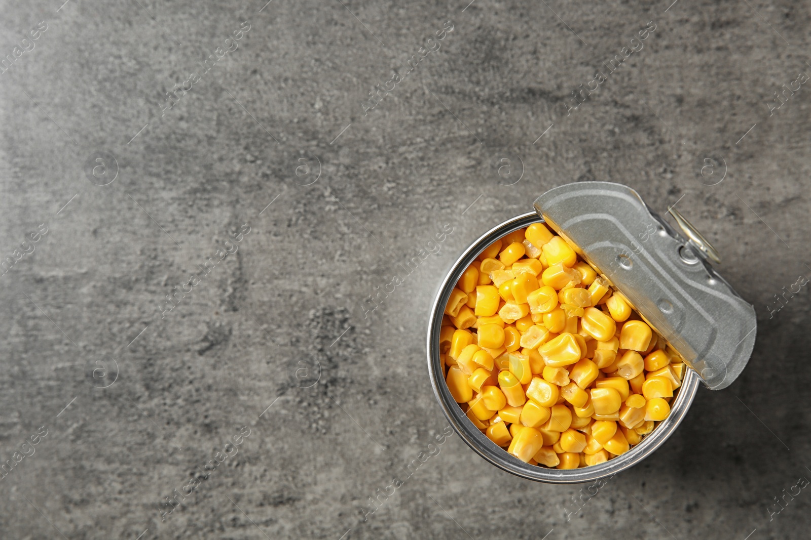 Photo of Open tin can of corn kernels on table, top view. Space for text