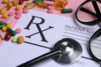 Photo of Medical prescription form, pills, glasses and stethoscope on pink background, closeup