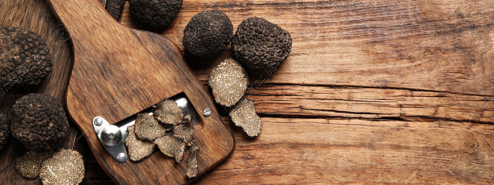Image of Shaver with whole and sliced black truffles on wooden table, flat lay with space for text. Banner design