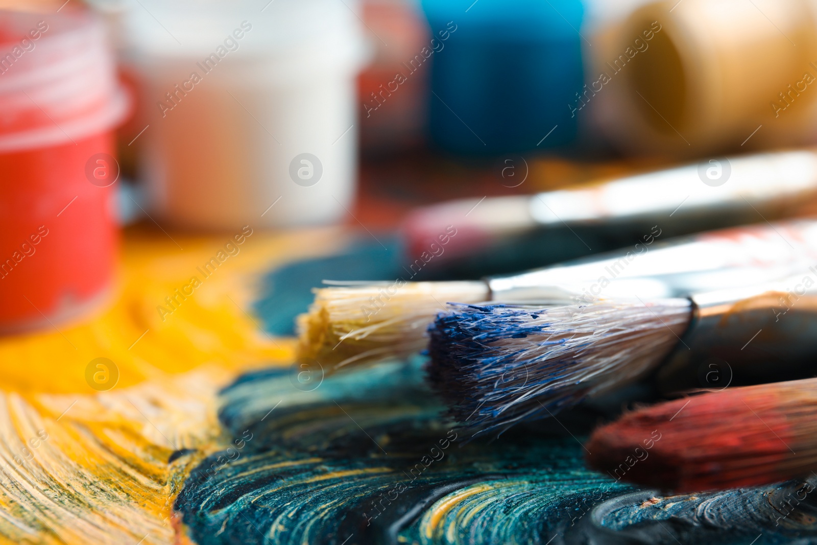 Photo of Different brushes and jars with paint on palette, closeup. Space for text
