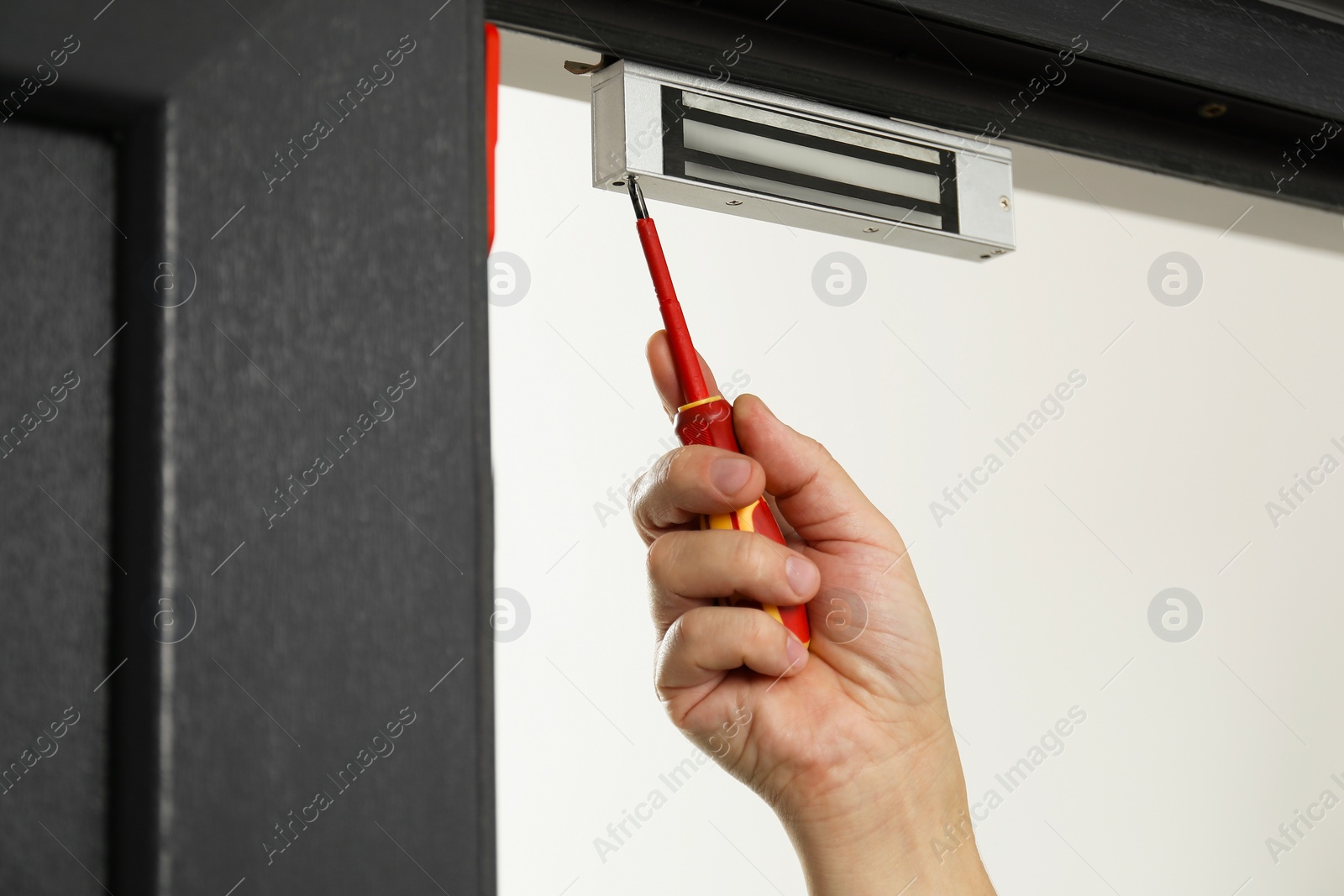 Photo of Man with screwdriver installing electromagnetic door lock indoors, closeup. Home security