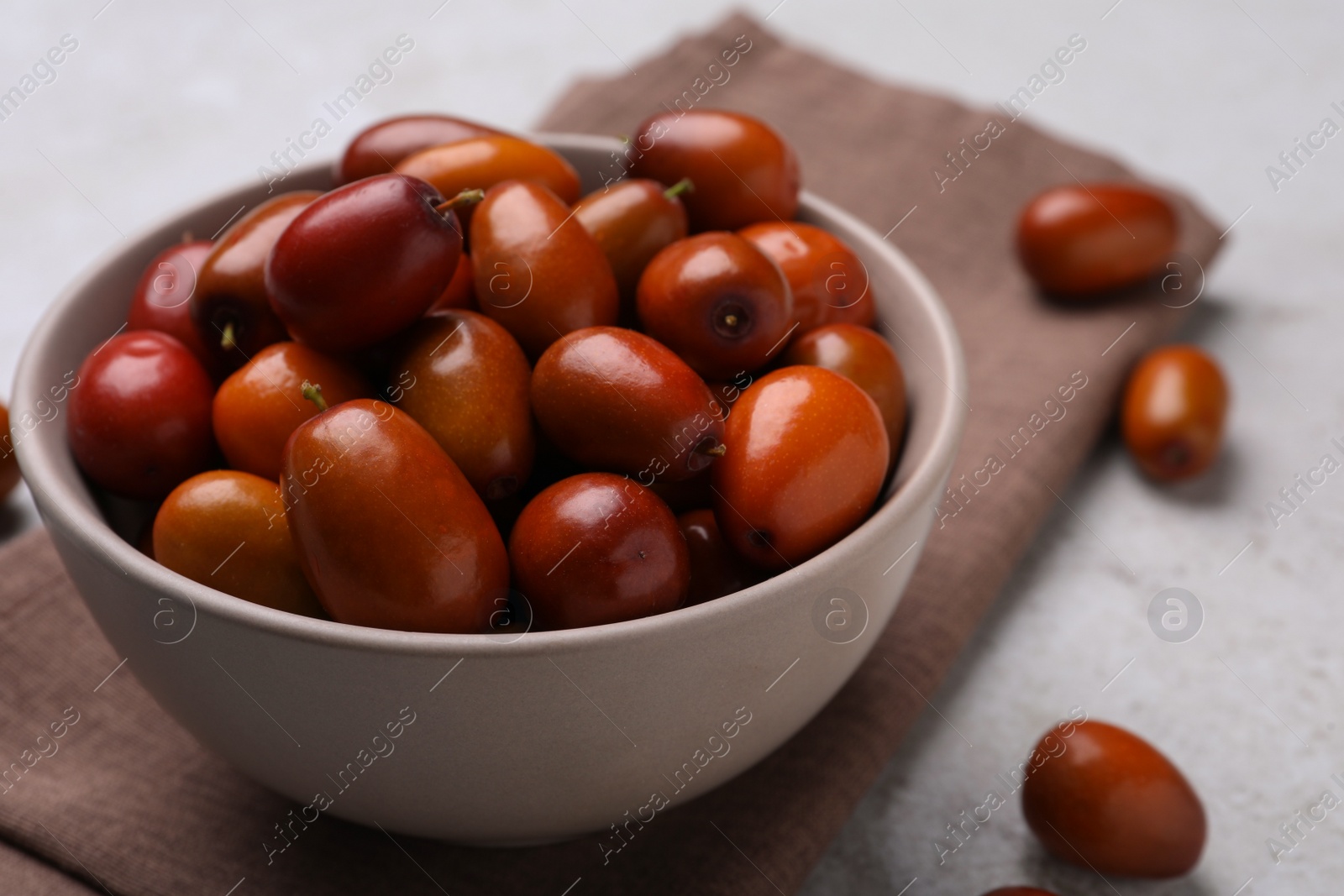 Photo of Fresh Ziziphus jujuba fruits with bowl and napkin on table, closeup