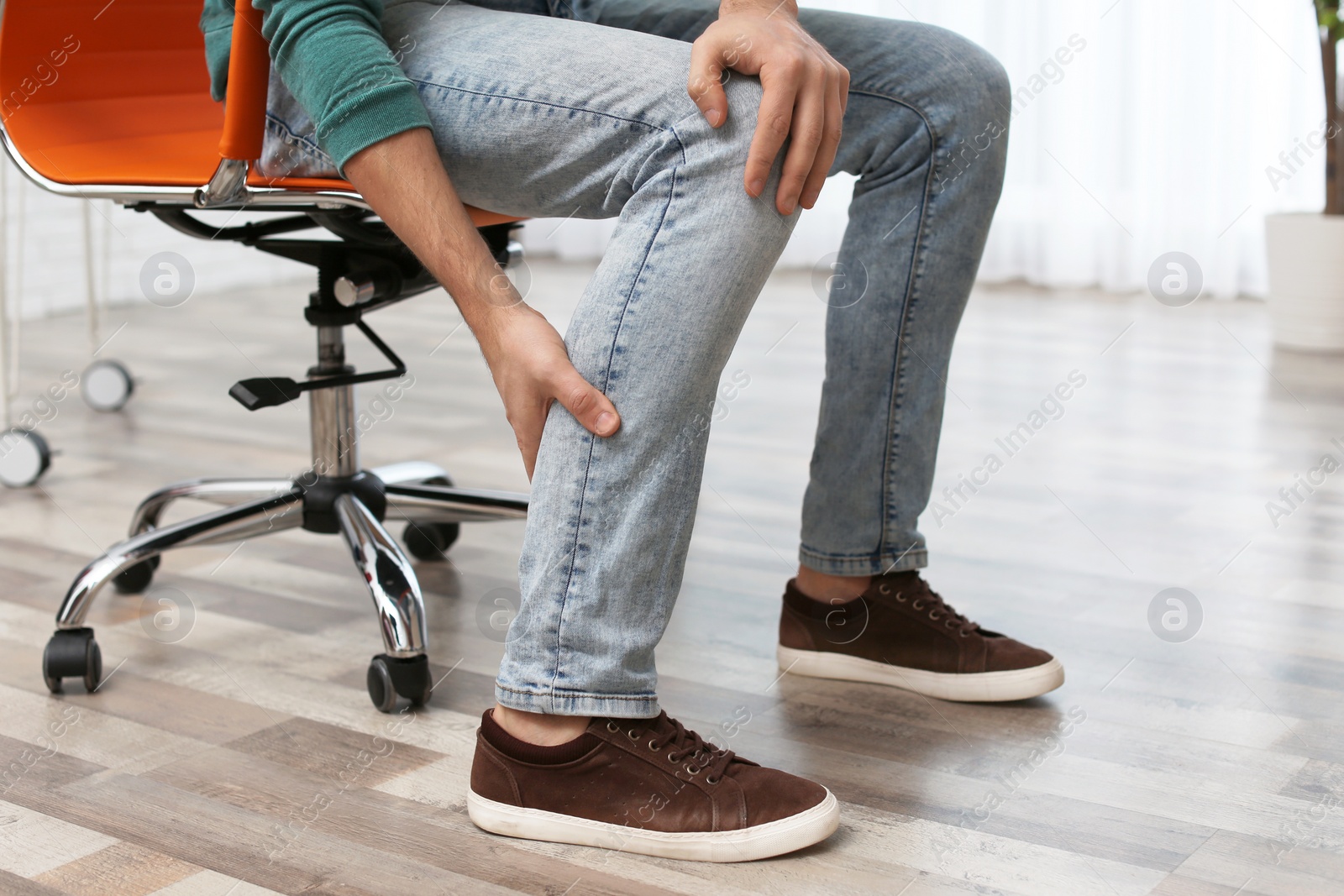 Photo of Man suffering from leg pain indoors, closeup