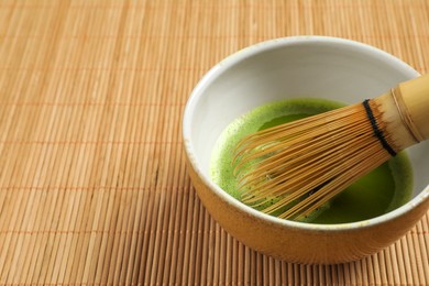 Photo of Cup of fresh green matcha tea with whisk on bamboo mat, closeup. Space for text