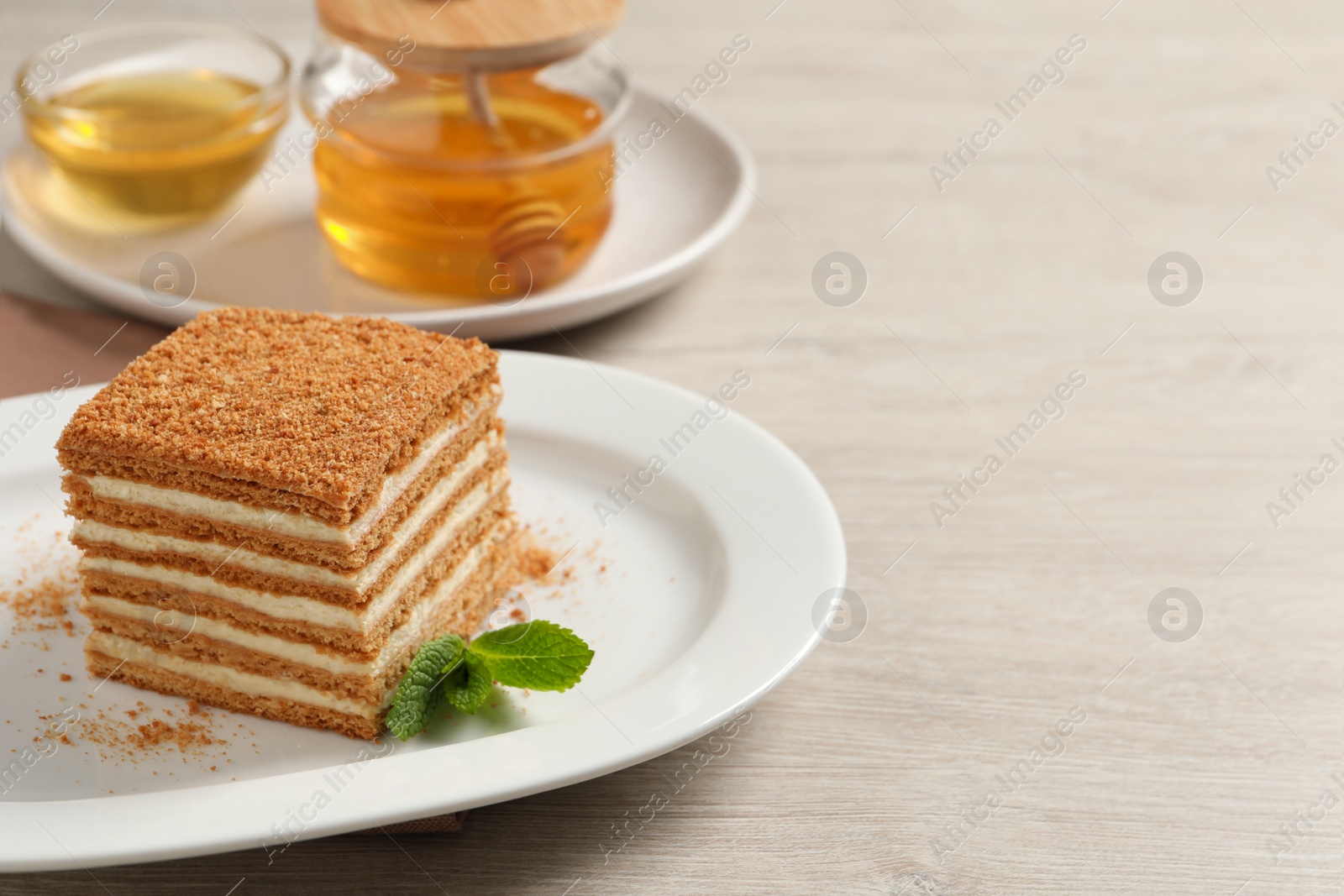 Photo of Slice of delicious layered honey cake with mint served on wooden table. Space for text