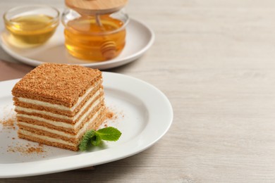 Slice of delicious layered honey cake with mint served on wooden table. Space for text