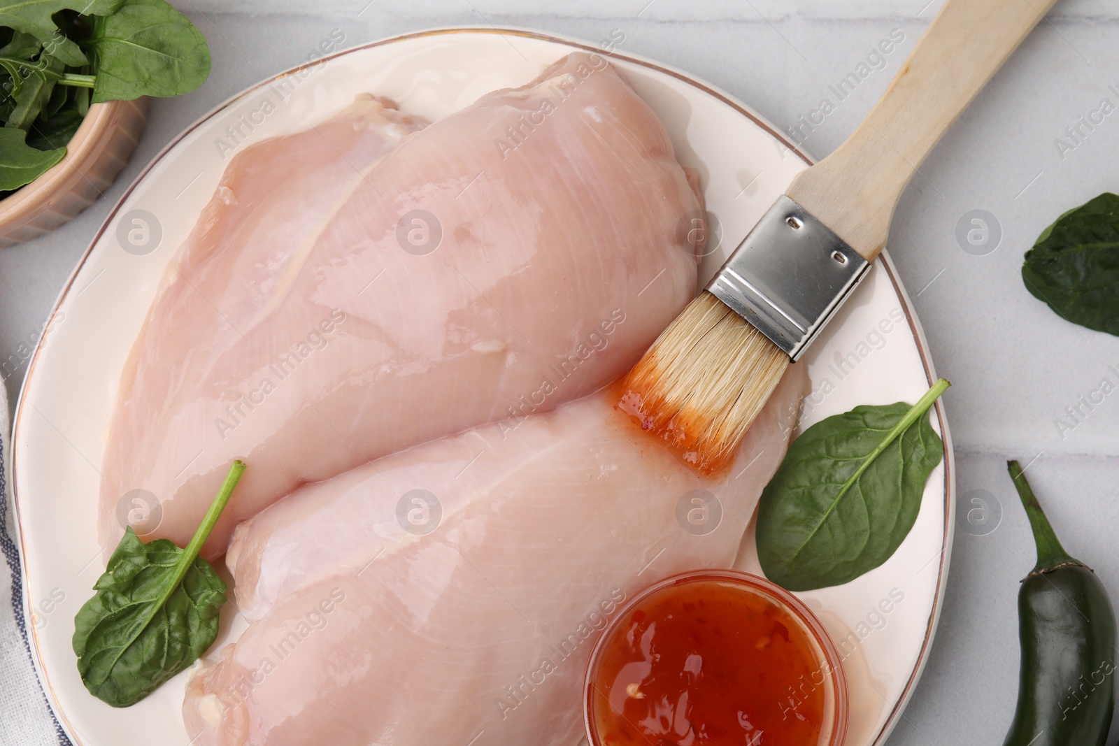 Photo of Marinade, basting brush and raw chicken fillets on white table, flat lay