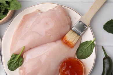 Photo of Marinade, basting brush and raw chicken fillets on white table, flat lay