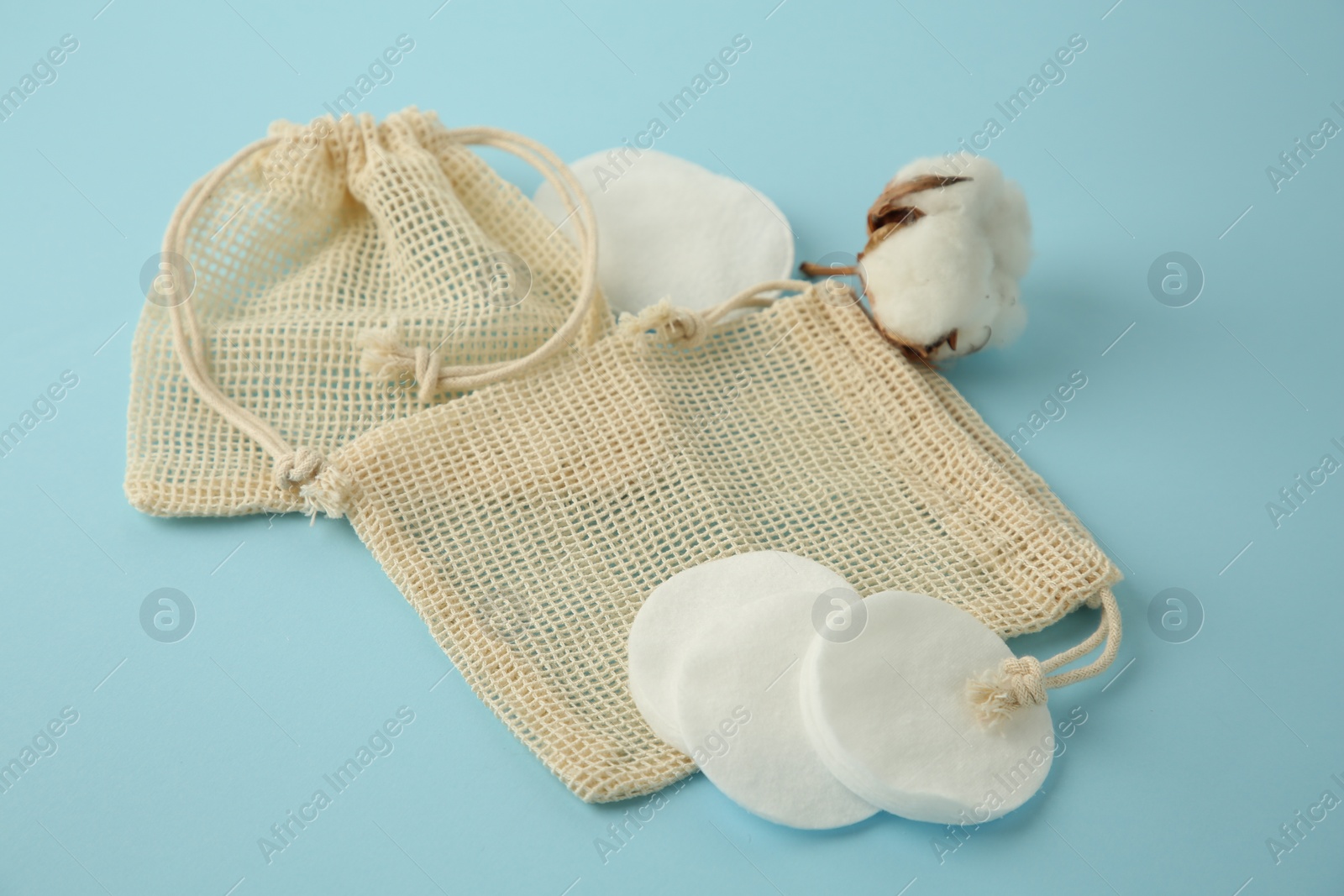 Photo of Bags, cotton pads and flower on light blue background, closeup