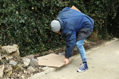 Poor homeless man with cardboard on street